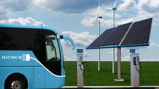 An electric bus is parked at a charging area with renewable energy sources at the background.